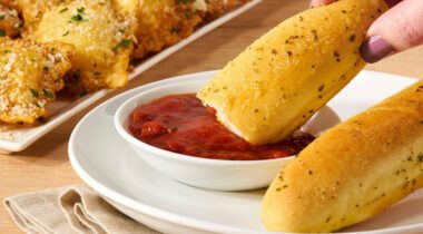 piece of garlic breadstick being dipped in marinara sauce