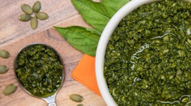 white bowl with green pesto sauce and spoonful of pesto sauce. image on wood surface