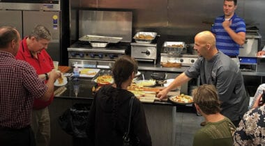 people gathered around an island in a kitchen with a chef