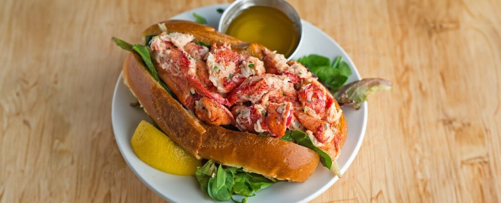 a lobster roll on a plate with butter and a lemon wedge