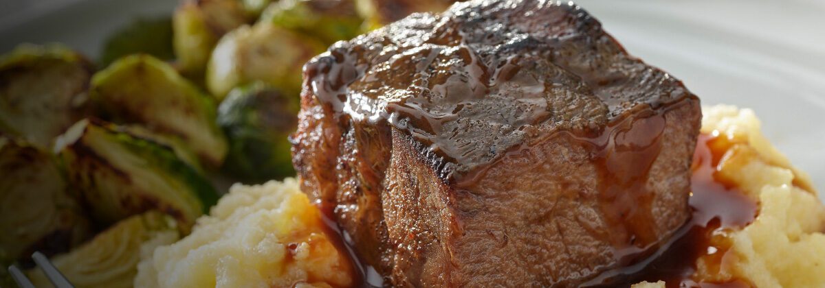 cut of beef on mash with gravy and Brussels