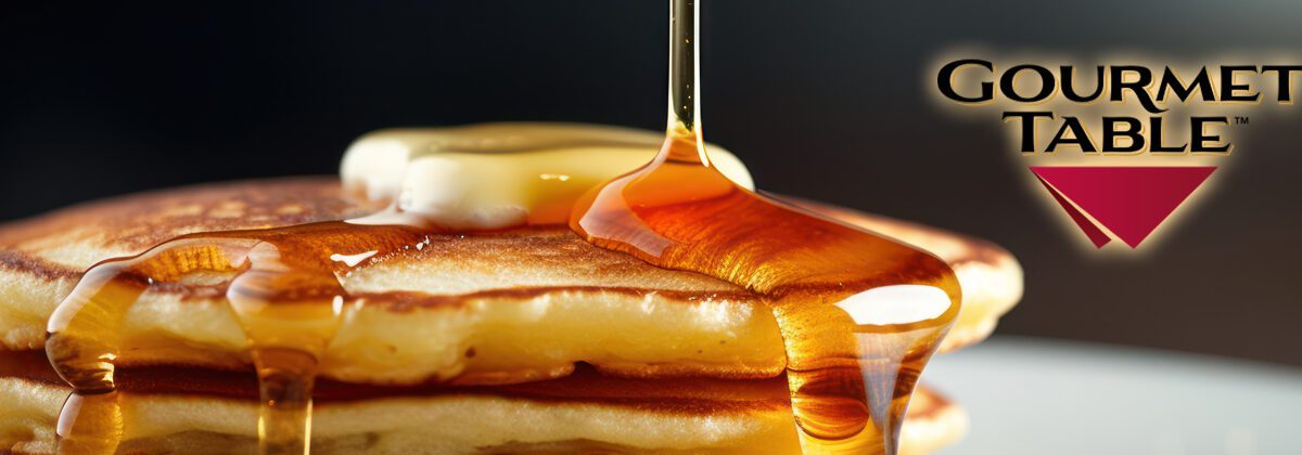 syrup being drizzled over pancakes and butter