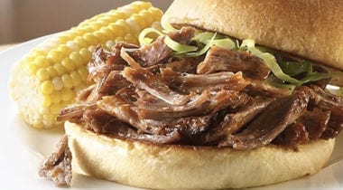 pulled pork on a bun with corn on the cob